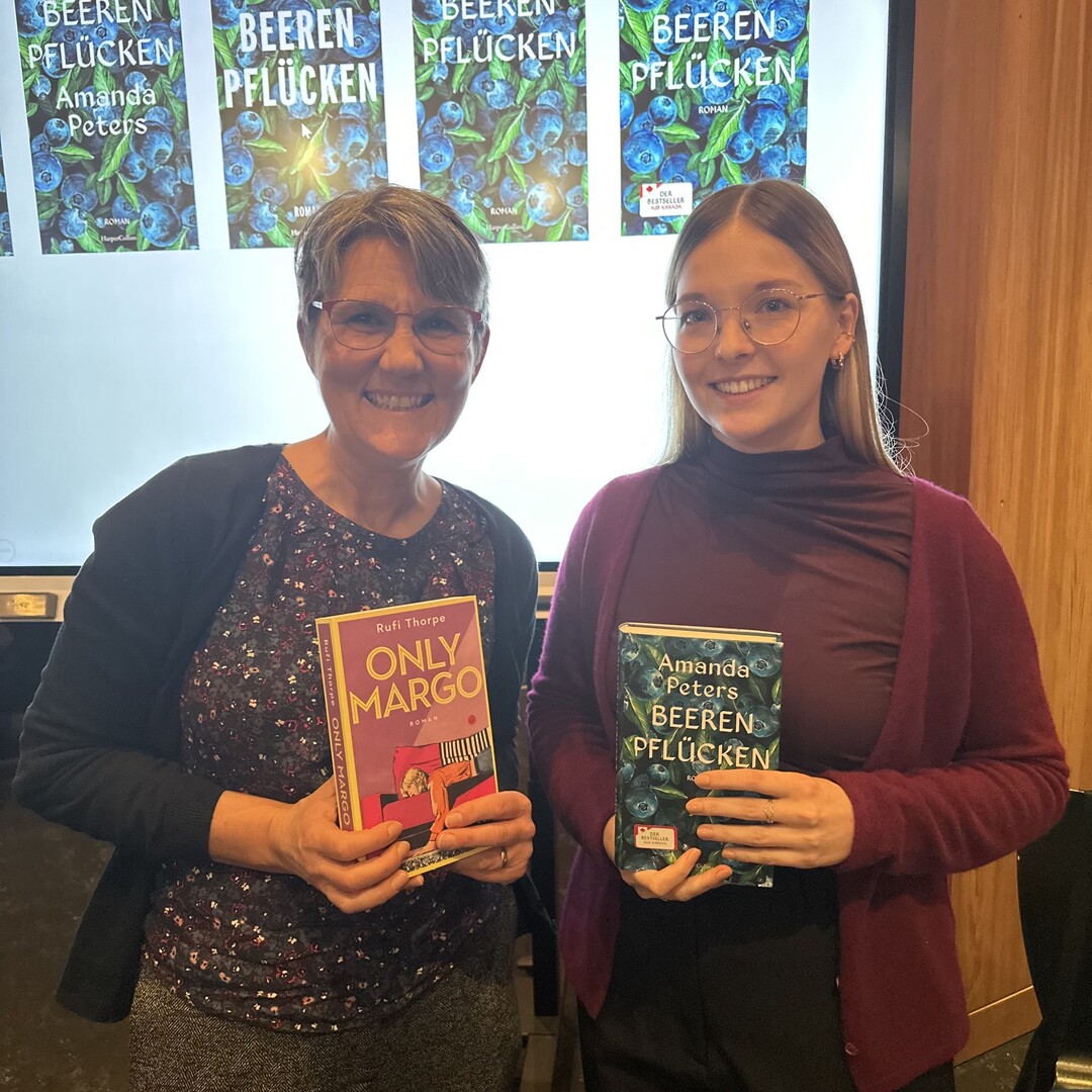 Frau Metzger und Frau Körber vom Verlag Harper Collins halten die Bücher "Only Margo" und "Beeren pflücken" in die Kamera und lächeln.