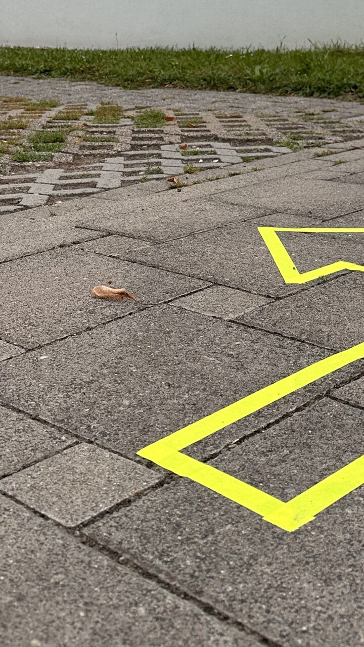 Draußen wurde auf einem Weg auf dem Campusgelände ein Pfeil mit neongelbem Klebeband geklebt. Er dient als Wegweiser.